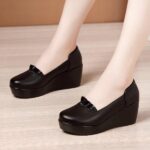 Photo of a pair of black wedge loafers worn by a woman on a parquet floor with a brown wall in the background