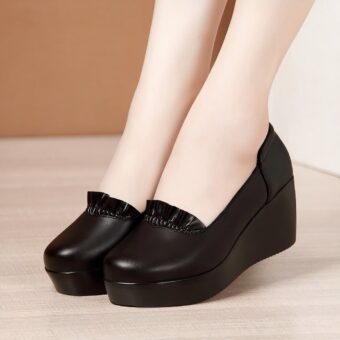 Photo of a pair of black wedge loafers worn by a woman on a parquet floor with a brown wall in the background