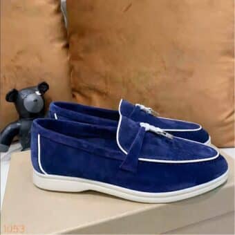 Moccasin in blue suede with white piping and a hard tassel on the front of the shoe which is placed on a shoe box