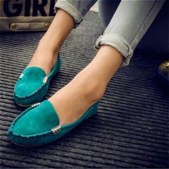 green suede moccasin worn by a woman sitting on the floor