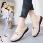 Photo of a pair of white moccasins worn by a woman with black jeans, on a gray floor with a woman in the background