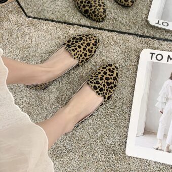 Pair of simple moccasins with leopard print seen from above worn with a white skirt and bare feet. The floor is beige carpet and there's a white magazine next to it