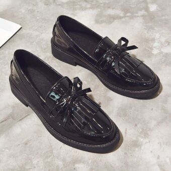 Pair of black patent loafers with fringe on a grey floor