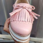 Photo of a pink fringed wedge loafer worn in front of a door
