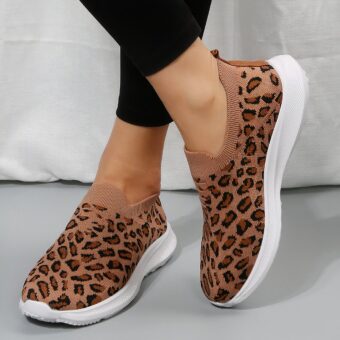 on a grey floor, a pair of sporty leopard-print moccasins with a thick white sole, worn bare-ankled with black leggings