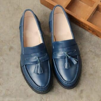 blue leather heeled moccasin with tassel on top, set on grey ground