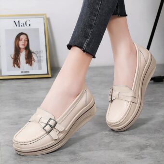 Photo of a pair of white wedge loafers worn by a woman in black pants on a gray ground