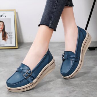 Photo of a pair of blue wedge moccasins worn by a woman in black pants on a gray floor