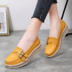 Photo of a pair of yellow wedge loafers worn by a woman in black pants on a gray floor