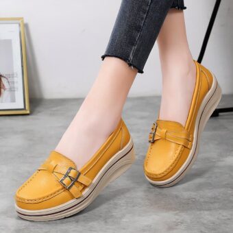 Photo of a pair of yellow wedge loafers worn by a woman in black pants on a gray floor