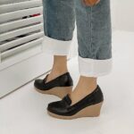 Photo of a pair of black wedge loafers worn by a woman in jeans on a gray floor