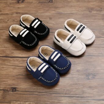 On brown parquet, three pairs of baby boat moccasins with topstitching, and two white bars on the top tongue. We see a white, blue and black pair