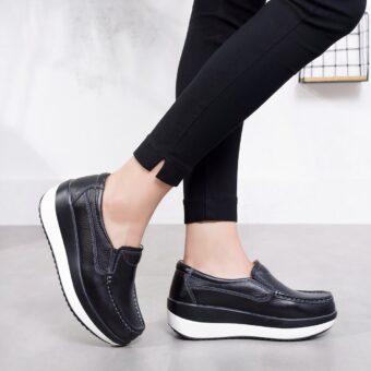 Photo of black orthopedic platform loafers with a white sole, worn by women's legs in black pants.