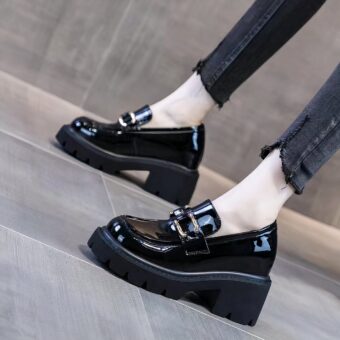 Black patent loafers with heels and thick black soles on the feet of a woman standing in black skinny jeans.