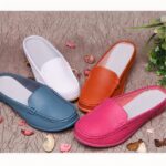 4 moccasin mules in blue, white, orange and pink with top stitching and white insoles. They are set on a beige ground with pink and beige flower petals all around