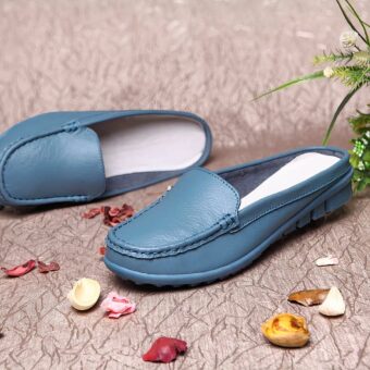 Pair of blue square-toed moccasin mules with traditional topstitching on a marbled fabric with colorful dried flower petals all around