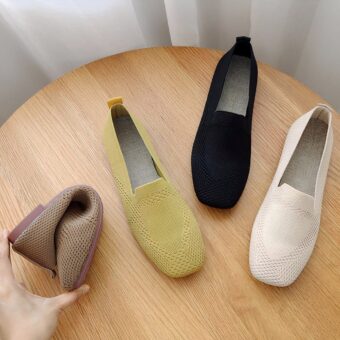 On a wooden table, 3 square-toed moccasins in yellow, black and beige mesh. A hand is seen folding a moccasin to show its suppleness