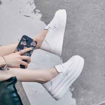 Feet in white moccasins with one hand holding a blue phone