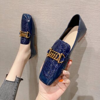 pair of moccasins in imitation leather, royal blue with a thick decorative gold chain, unn moccasins worn one in a hand, on a beige background
