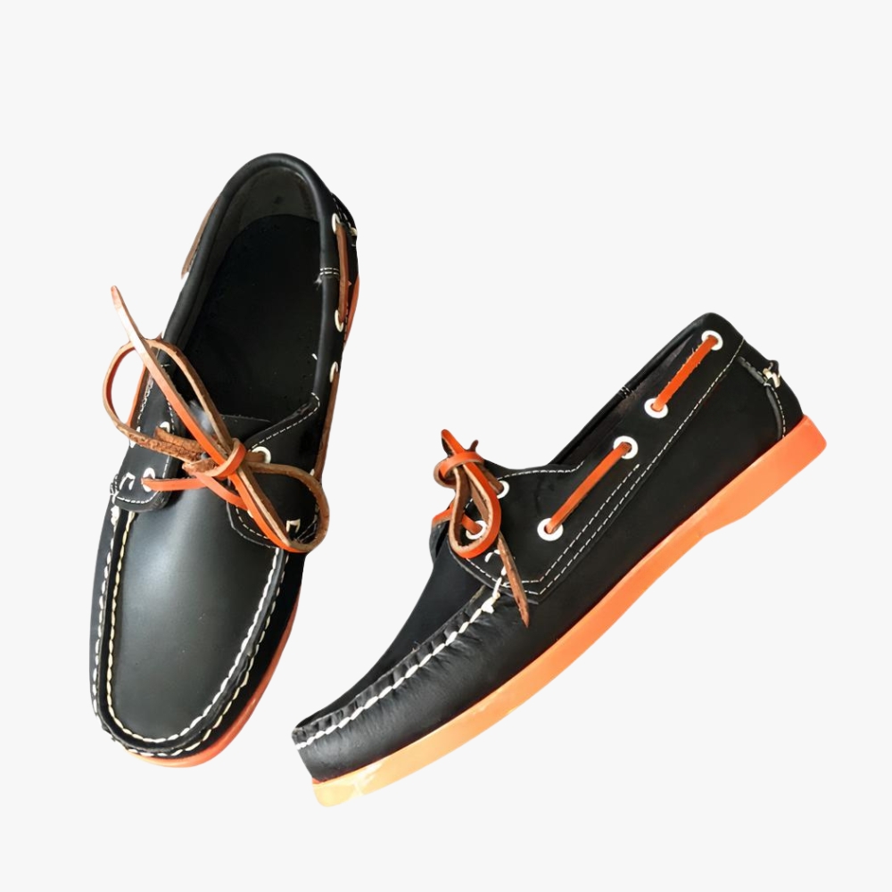 Black boat loafers with orange soles, placed on a grey sofa