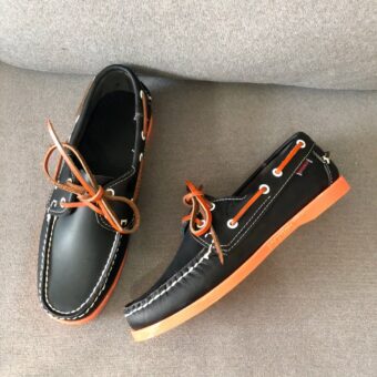 Black boat loafers with orange soles, placed on a grey sofa
