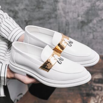 White patent leather tassel loafers for men with a grey background and a woman holding the loafers in her hands