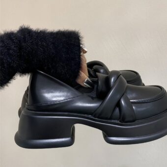 Women's black platform loafers in synthetic leather with beige background and a woman holding the pair of shoes