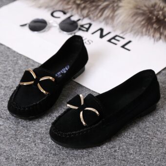 Pair of black moccasins with a gold bow on the floor with accessories around them