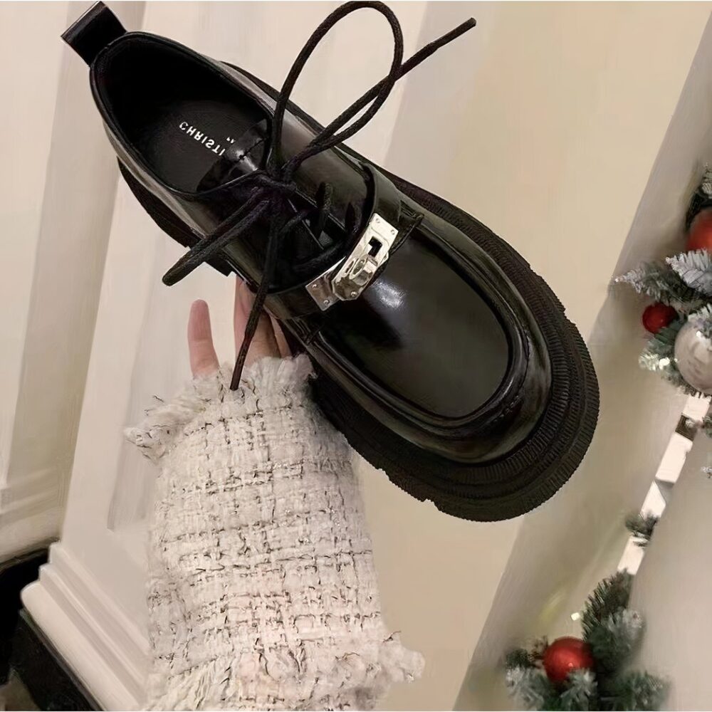 Hand of a woman holding a black lace-up moccasin, in the room of a house