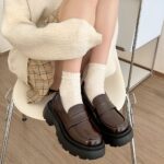 Leather platform moccasins in punk style for women with a background of a woman sitting in a chair with the moccasins