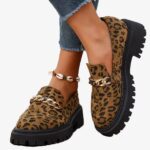 Leopard suede and chain loafers worn by a woman on a white background