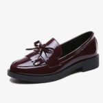 A patent loafer with fringe and bow in red on a white background