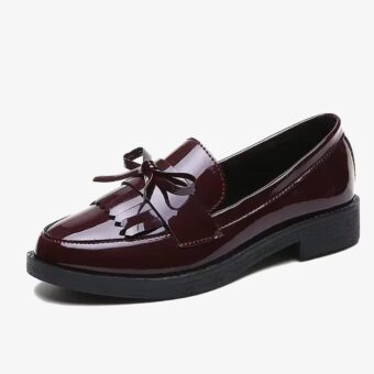 A patent loafer with fringe and bow in red on a white background