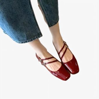 Woman's feet wearing patent ballerina loafers with double buckles in red with blue jeans on a white background
