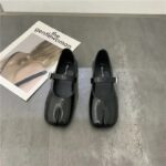 Pair of black split leather Mary Jane ballerinas for women - Tabi style on a grey floor in front of a magazine