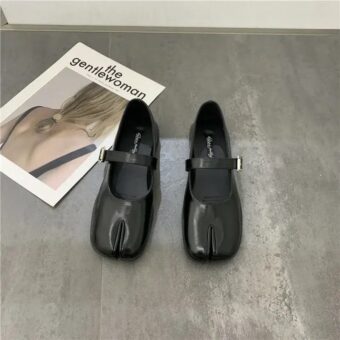 Pair of black split leather Mary Jane ballerinas for women - Tabi style on a grey floor in front of a magazine